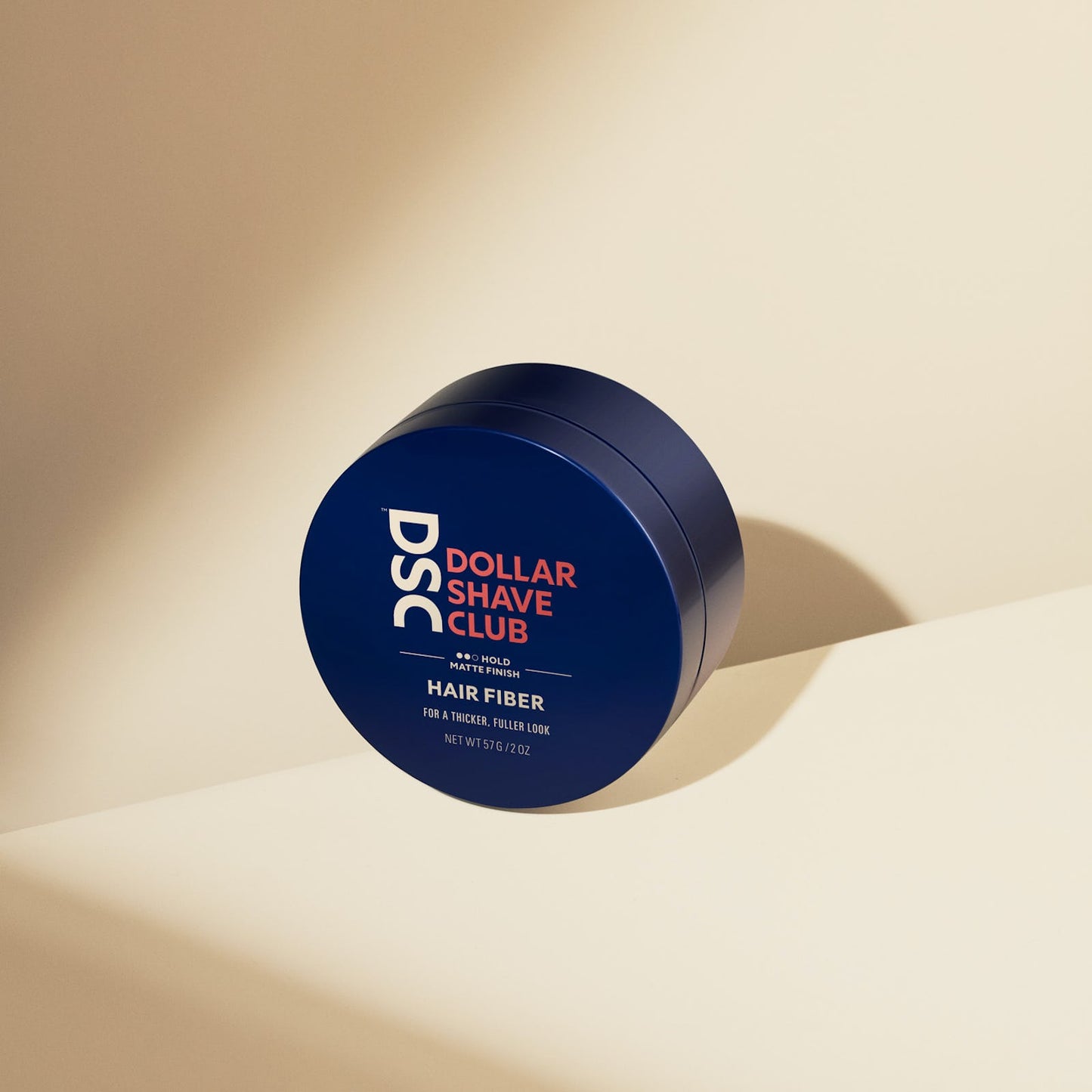 Dollar Shave Club Hair Fiber against tan backdrop.