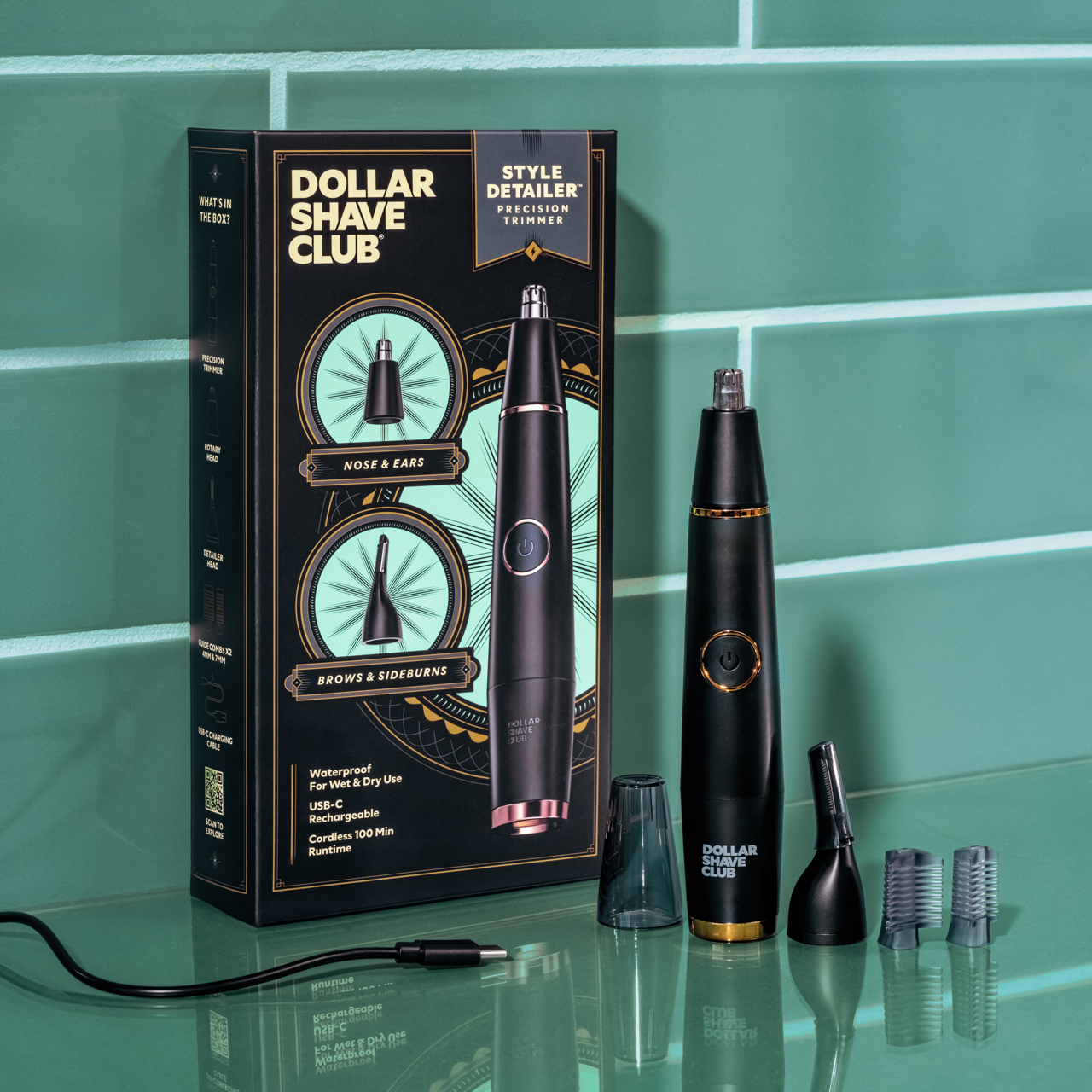 A photo of the Style Detailer, the box, and everything that is included in the box; 3 different styling heads, charging cable, and protective cap. All against a teal green tile bathroom.